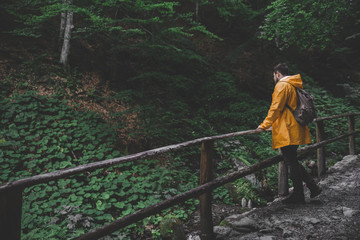 man walking by forest trail to waterfall in yellow raincoat