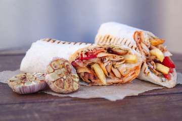 Shawarma sandwich gyro- fresh roll of thin lavash (pita bread) filled with grilled meat, mushrooms, cheese, cabbage, carrots, sauce, green. Traditional Eastern snack. On a wooden background
