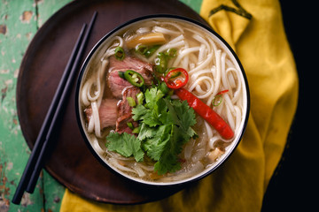 Vietnamese traditional soup Pho Bo with beef and fresh coriander on rustic wooden table