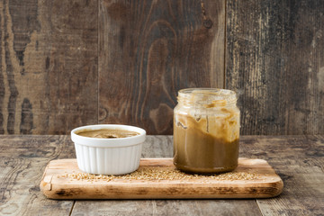Tahini and sesame seeds on wooden table. 
