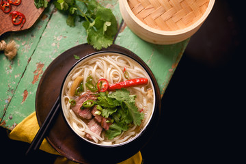 Vietnamese traditional soup Pho Bo with beef and fresh coriander on rustic wooden table