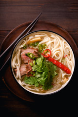 Vietnamese traditional soup Pho Bo with beef and fresh coriander on dark wooden background