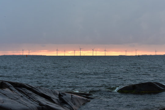 Gray sky, gold horizon, turbines, sea, and rocky shore in Kallo Island in Pori, Finland