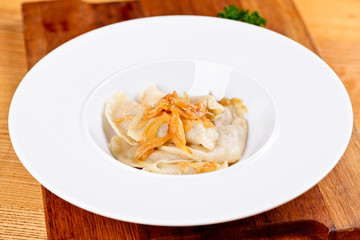 Dumplings filled with potato and topped with fried onion on white plate. Varenyky, vareniki, pierogi, pyrohy