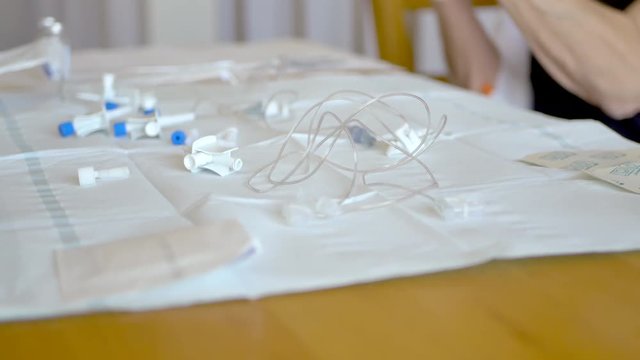 Middle aged woman preparing vials of antibiotic solution with tubes and various medical equipment strewn about the table for an at home infusion treatment.