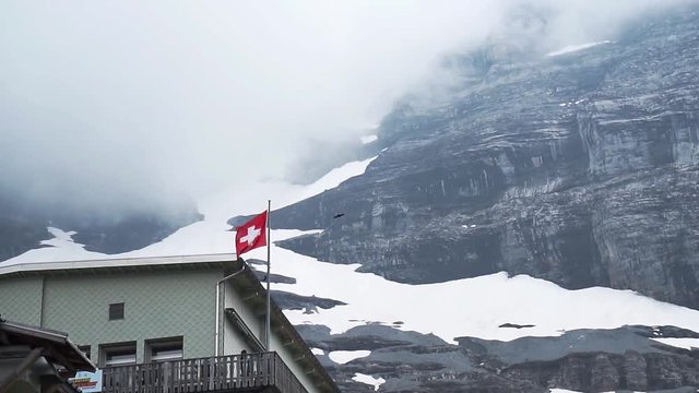 Swiss Flag waving dramatically with birds flying in slow motion at Eigergletscher mountains