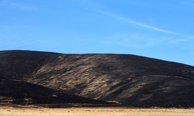 California drought parched brown fields with fire scorched hills in the background. Blue cloudy sky.