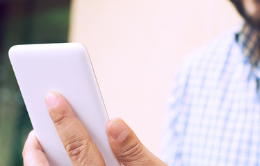 Cropped image young man sitting at the table with cup of coffee and smart phone, man's hands typing message on phone touch screen while sitting on balcony terrace.