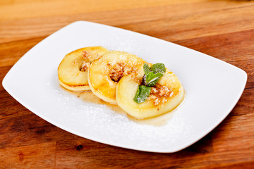 Baked apple rings with walnuts and honey on white plate. Autumn dessert. Close up