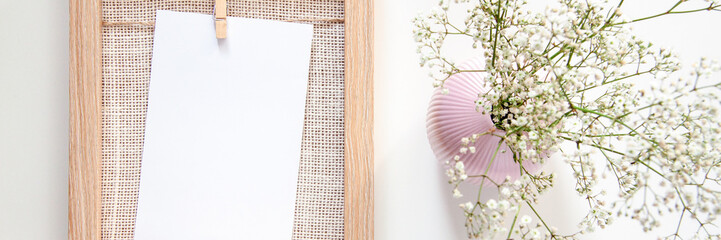 Panoramic photo with a wooden frame with a white card and a pink vase with sombre field flowers