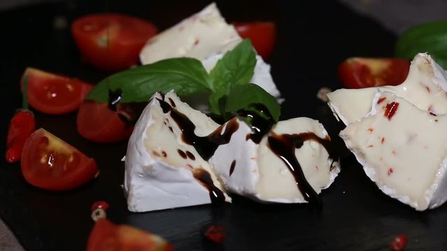 Pouring balsamic vinegar cream over Camembert cheese with pepper and chili peppers on a dark slate