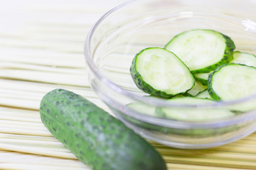 Cucumber home spa and hair care concept. Sliced cucumber, bottles of oil, bathroom towel. Straw light background