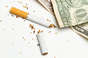 Cigarrillo roto por la mitad y dolares. Vista superior. Concepto: Adicción