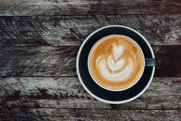 Top view of hot coffee latte cappuccino cup on dark gray ceramic saucer with latte art milk foam on rustic wood planks table background.