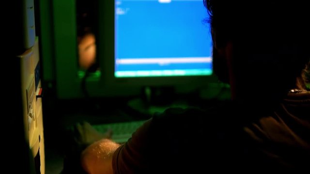 Hacker works in dark room with old retro PC types commands by console