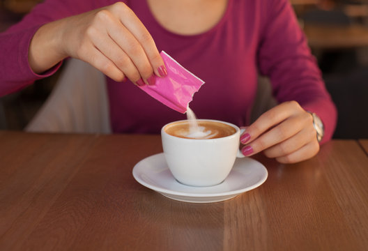 Young woman adding sugar in coffee