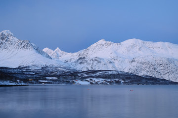Landscape of Norway in winter during blue hour. Norwegian coastline in winter. Mountain covered with snow at the background.