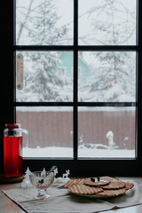 The concept of home winter comfort.  Delicious crispy homemade waffles with jam in a glass bowl on the table near the winter window. In the background lights Christmas garland.