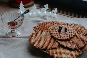 Homemade waffles with jam and a jug with a red drink on the table by the winter window.