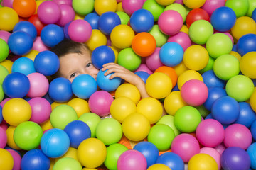 Cute smiling boy in sponge ball pool looking at camera. Child playing with colorful balls in...