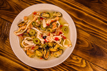 Ceramic plate with different sea food and olives on wooden table. Top view