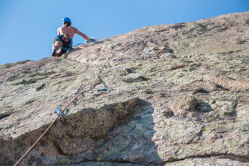 From below shot of shirtless male climber climbing out of focus on the mountain wall on an amazing sunny day 