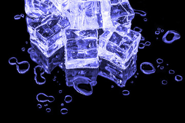 A hill of lilac ice cubes on a black glass with water drops around.