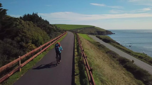 redhead woman cycling along the ocean coast. Waterford Greenway in Ireland 