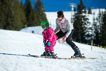 Mother and little child skiing in Alps mountains. Active mom and toddler kid with safety helmet, goggles and poles. Ski lesson for young children. Winter sport for family. Little skier, swiss Alps