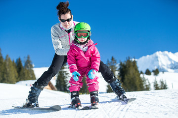 Fototapeta na wymiar Mother and little child skiing in Alps mountains. Active mom and toddler kid with safety helmet, goggles and poles. Ski lesson for young children. Winter sport for family. Little skier, swiss Alps