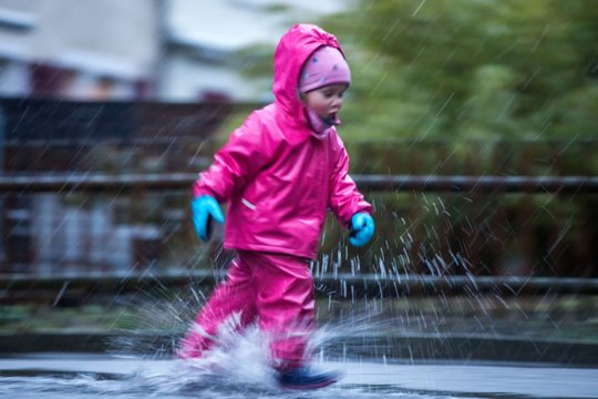 Girl is having fun in water on street in cold autumn day, girls splashing water in rain, happy and cheerful girl enjoying cold weather, kid in pink rain coats and rubber boots, running in rain