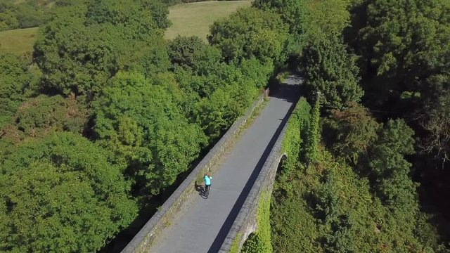 Aerial view of woman casually cycling across old railway bridge. Waterford Greenway.