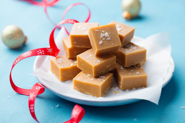 Fresh caramel fudge candies on a plate with Christmas red ribbon on blue background. Close up.