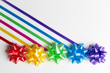 Pink, yellow, red, green, blue and purple gift wrap bows with diagonally placed ribbons top view on white background