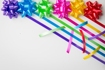 A top view of pink ,yellow, red, green, blue and purple gift wrap bows with diagonally placed ribbons  and ribbon cuts on white background