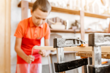 Little talented genius boy works with wood in a carpentry workshop. The concept of learning, hobbies and manual hand work for children