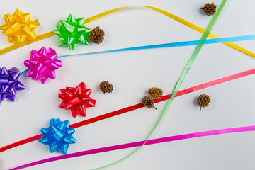 A top view of pink, yellow, red, green, blue and purple gift wrap bows with free lying ribbons and small dry plants  on white background