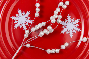 A top view of a christmas red plate with white ornaments: white twigs and snowflakes
