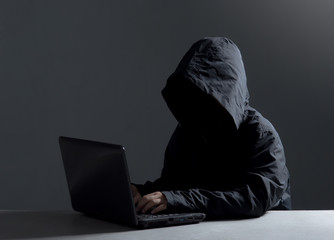 Hacker with hidden face in a hoodie using a laptop