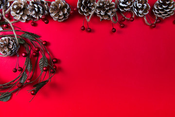A top view of a christmas ornaments: pine cones and circled twigs with red berries on red background