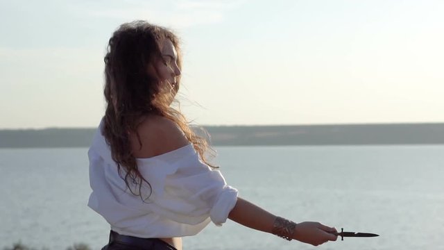Curly Gipsy brunette girl juggles with dagger knife on the slope of Gulf