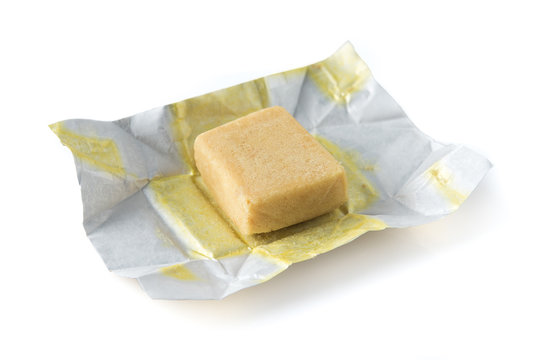 Bouillon stock broth cube in opened paper wrapping over white background