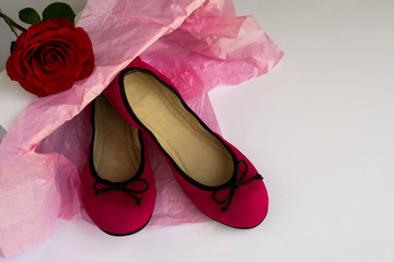 Pair of red female flat shoes in box, red rose on the white background. Copy space.