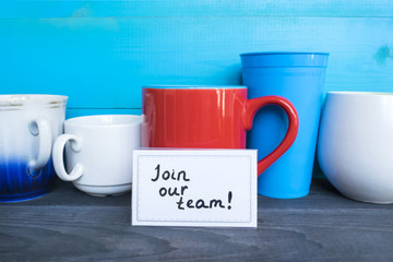 Red mug with words Join our team on the wooden table.