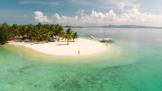 Aerial drone shot over People, Paraw boats and palm trees, on a tropical, paradise isle, in turquoise sea, at Pass island, in Philippines, Asia