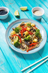 Asian tofu soba noodle bowl on blue wooden background.