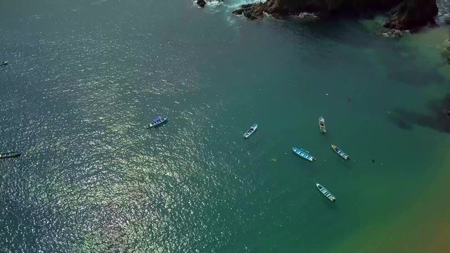 Fishing boats next to the sandy beach in green-blue waters of a sea - tilt up, aerial shot