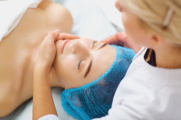 Beautician makes facial massage to a young woman in the spa salon.