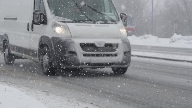 SLOW MOTION, DOF: White van drives down the slick road during an intense blizzard. Snowflakes falling from the sky making the asphalt street slippery and dangerous for the drivers on cold winter day.
