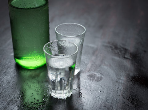 Alcoholic clear distilled korean Soju bottle with shot glass on a wooden background.